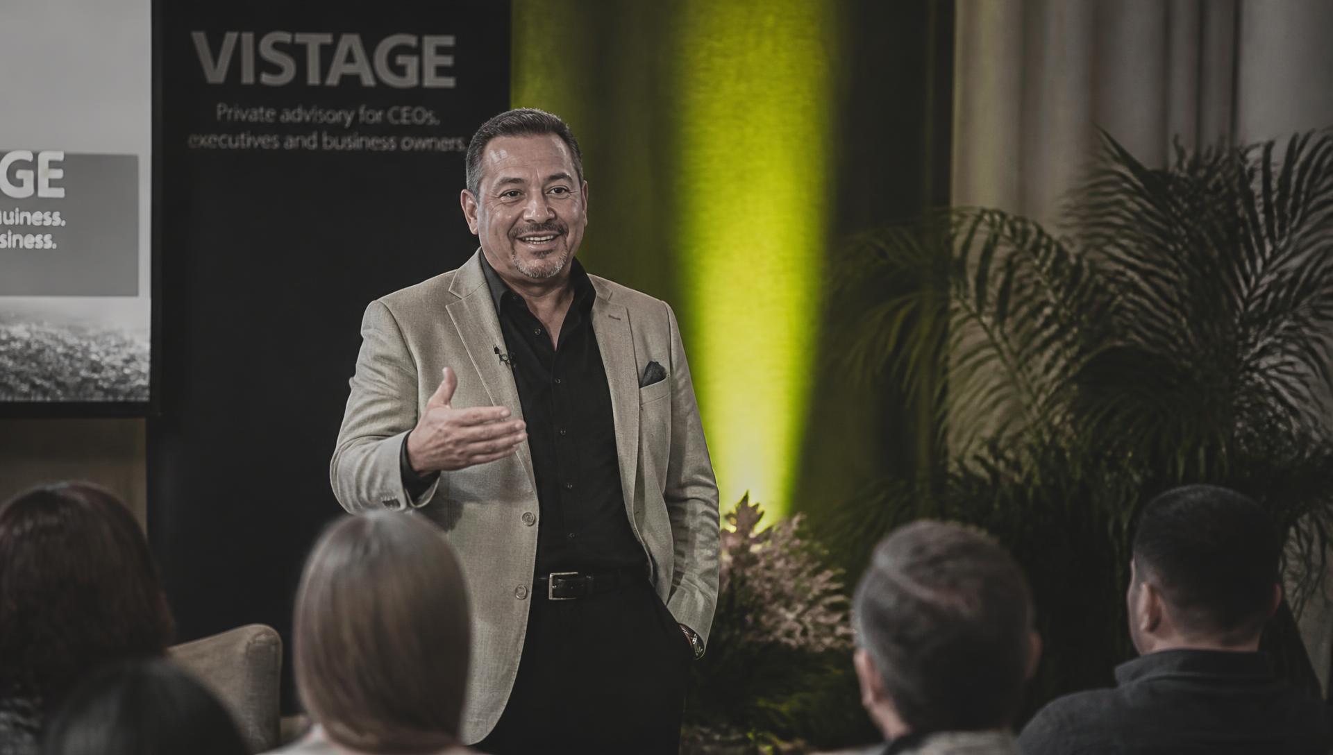 A business owner speaking on a small stage to a seated audience