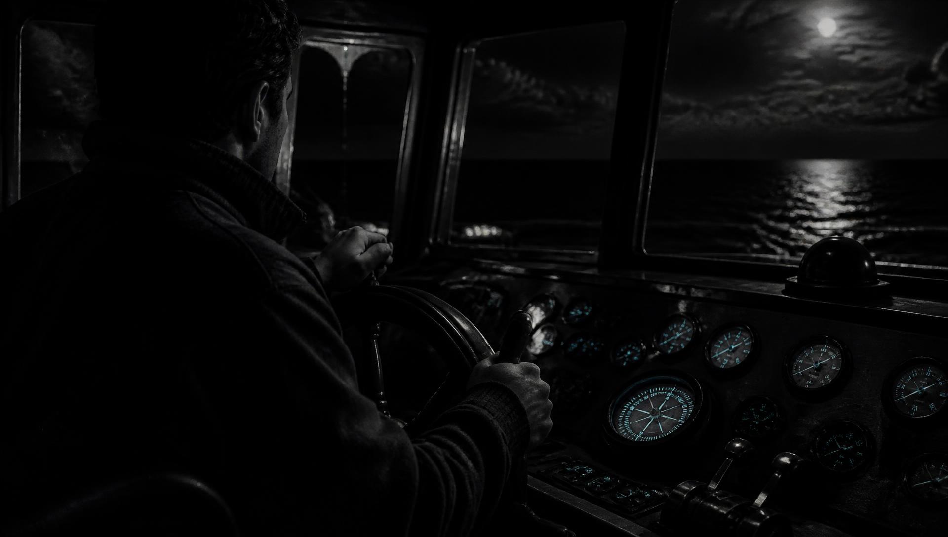 Hands on a ship's helm in a darkened wheelhouse, instruments softly lit