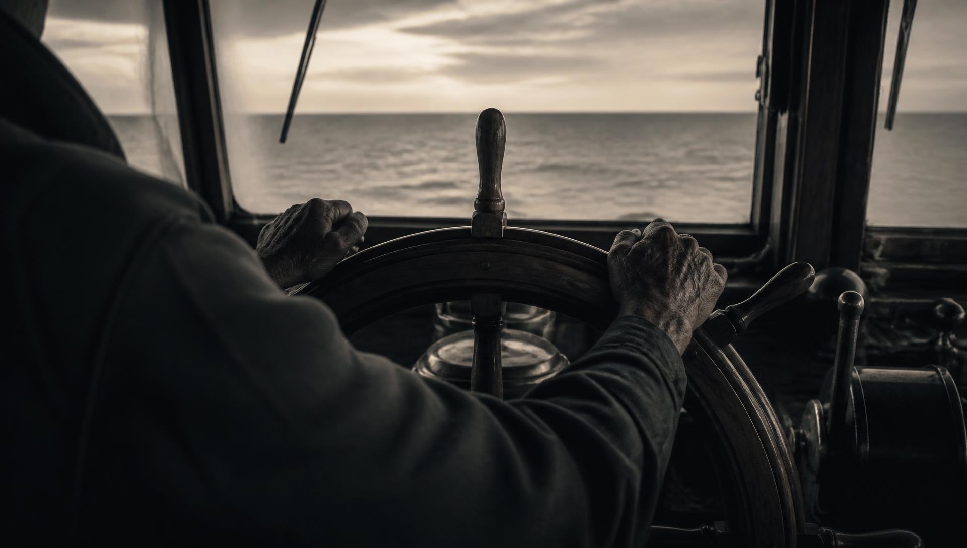 Hands resting on a ship's wheel with an open horizon ahead